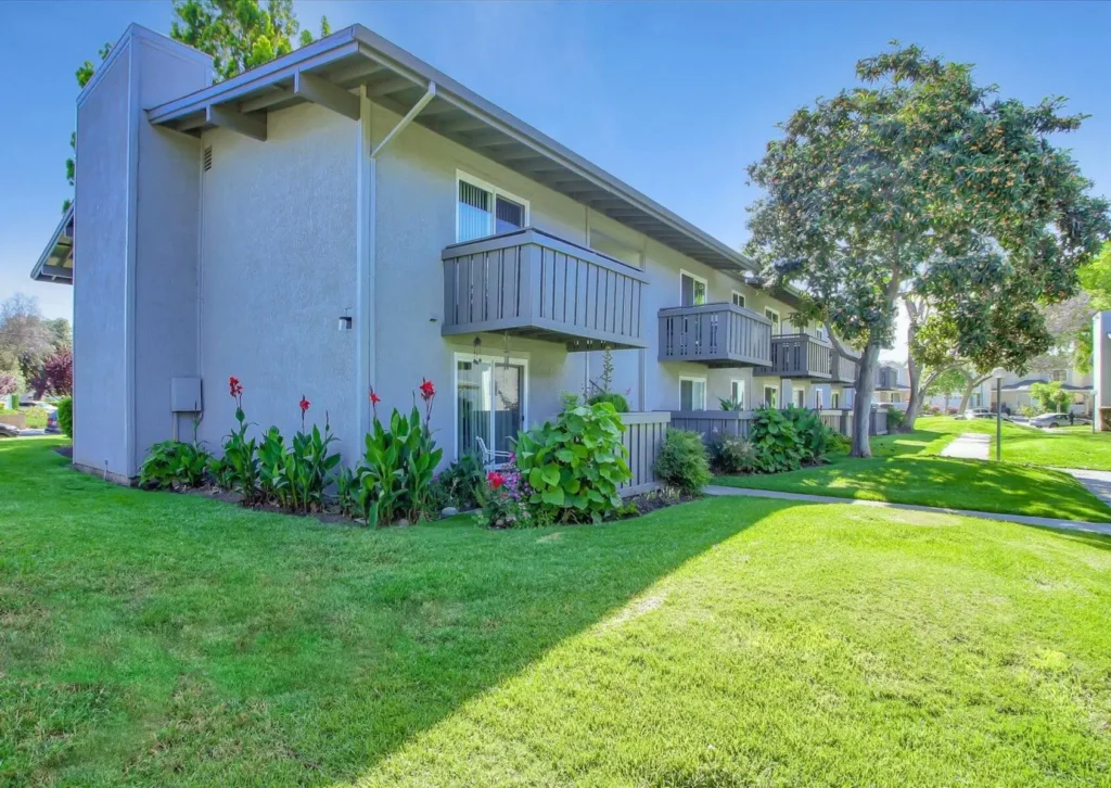 Building exterior with balconies and patios, lots of landscaping and trees around the building