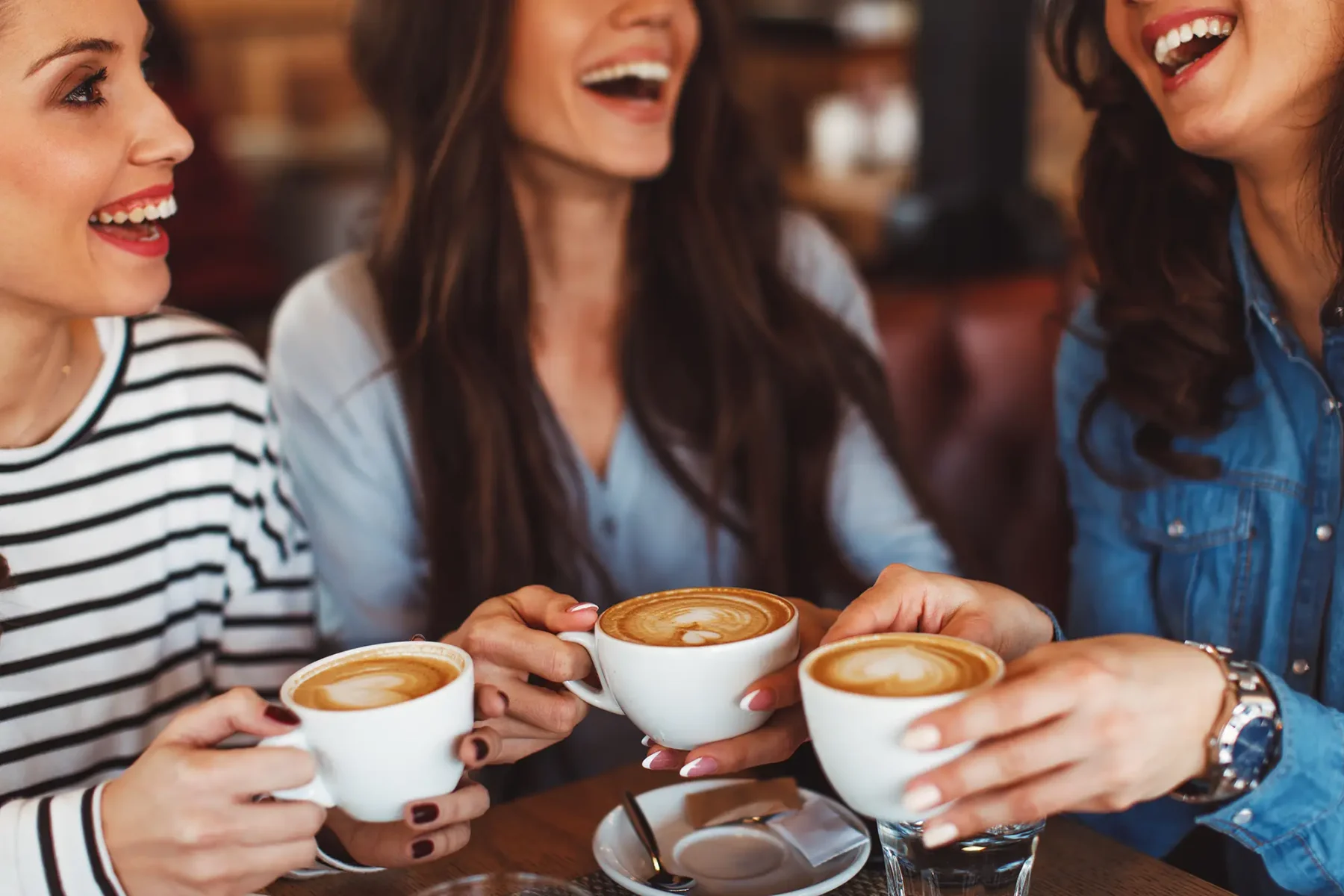 Women laughing in a cafe sitting at a table with coffee