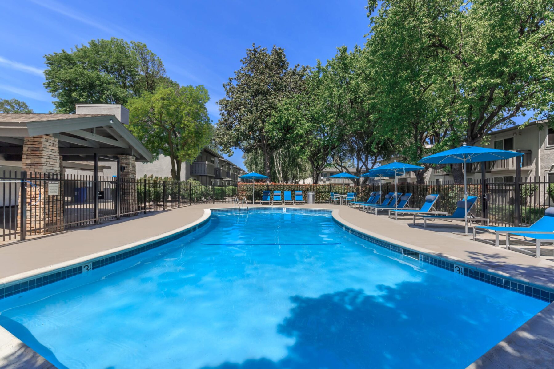 Fenced pool with deck chairs, umbrellas, and adjacent covered pavilion